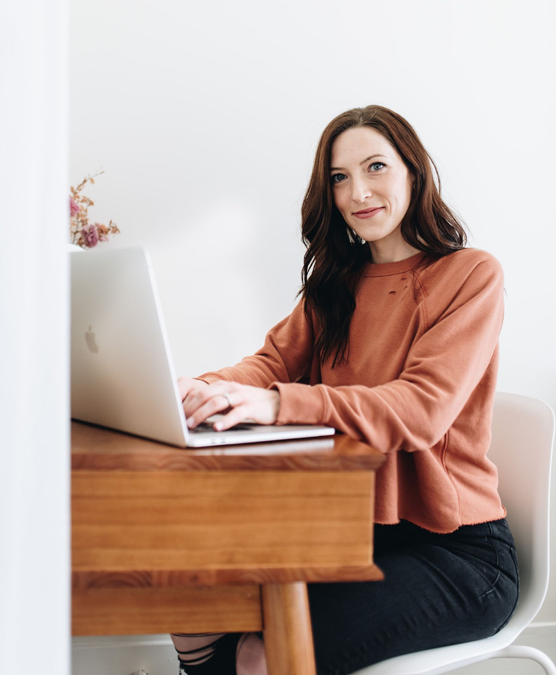 Woman typing on a laptop at a wooden desk, using a website builder for photographers in a bright, minimal space.