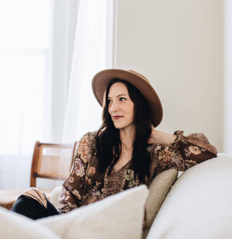 Woman sitting on neutral-toned couch wearing floral blouse and hat, representing premium Showit templates style.