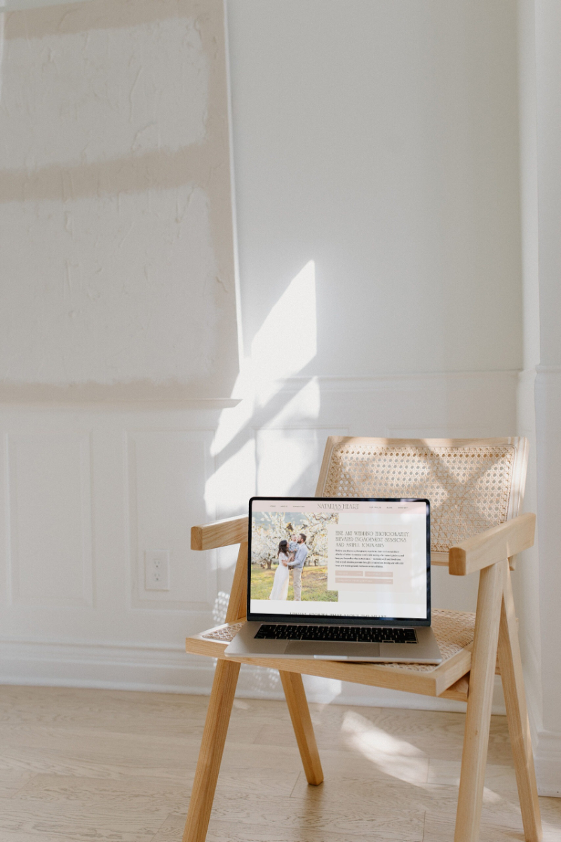 Laptop displaying a photography website, placed on a wooden chair in a softly lit room.